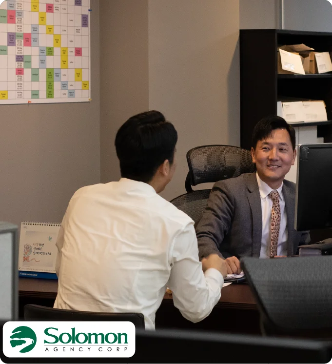 man in a suit talking to a client across a desk with the Solomon Agency logo.