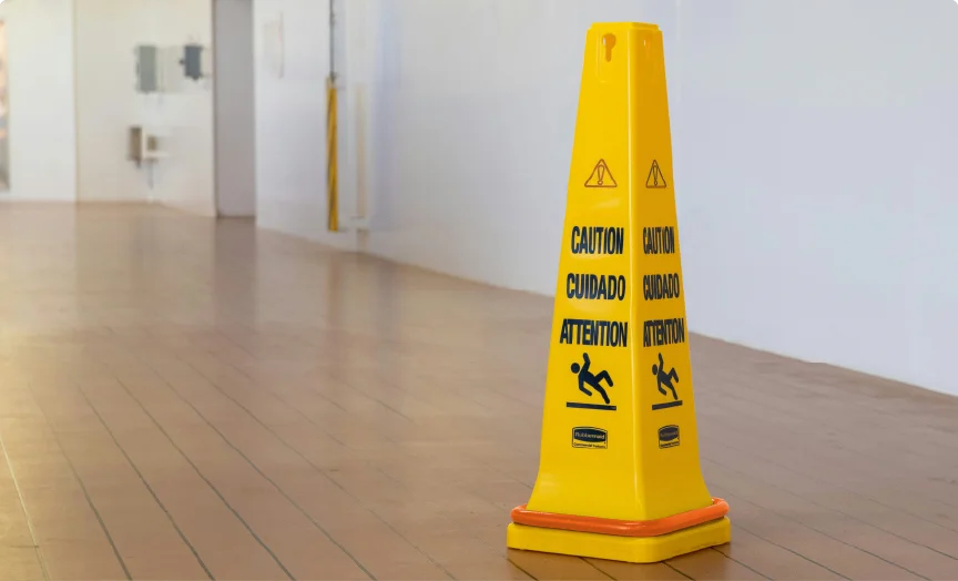 A yellow caution wet floor cone on a wooden floor.