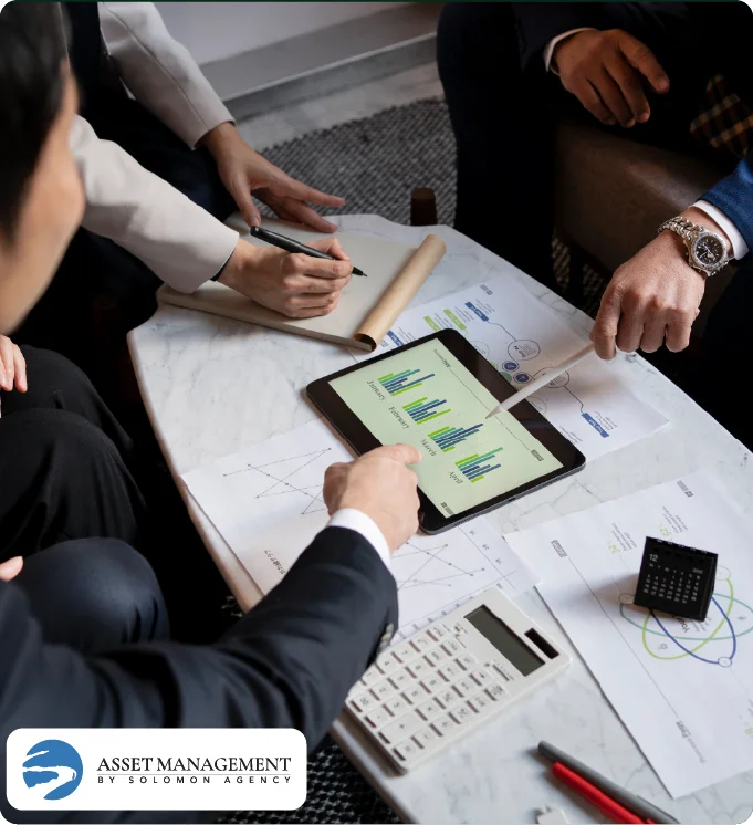People analyzing charts on a tablet and paper on a marble table with Solomon Asset Management logo.