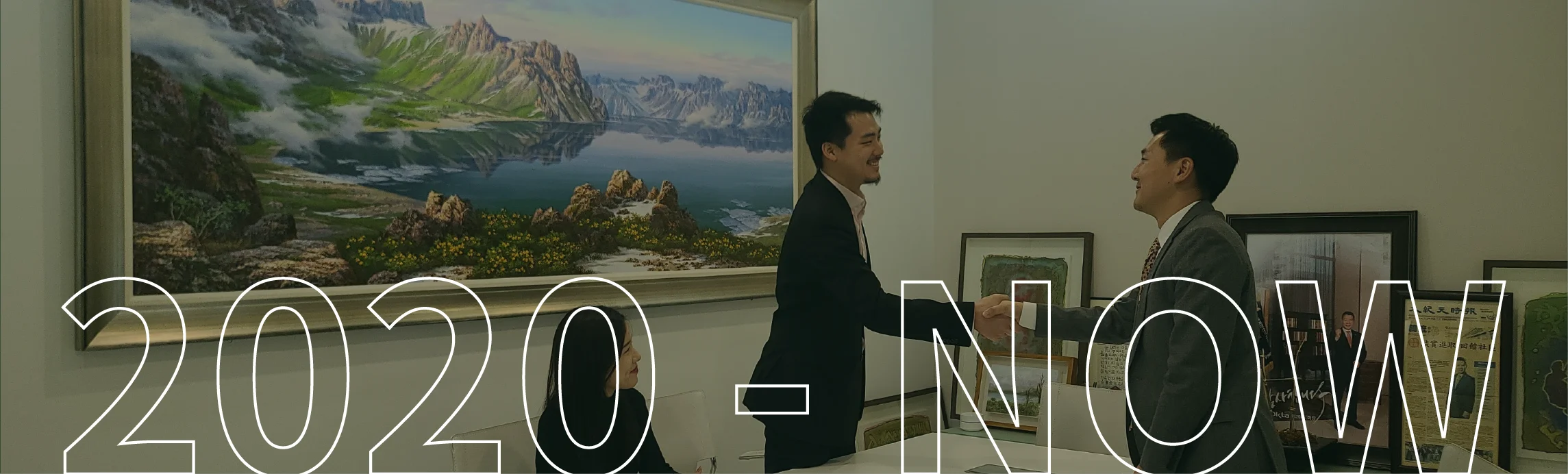 Two businessmen shaking hands in an office with the text "2020 - NOW" overlaid.