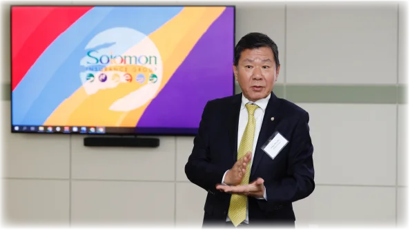 A man in a suit giving a presentation in front of a colorful screen.