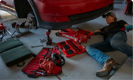 A mechanic working under a red car using professional tools in a garage.