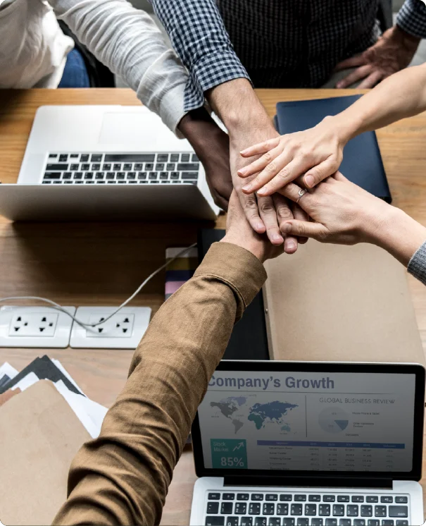A top-down view of a business team stacking their hands together over a laptop.