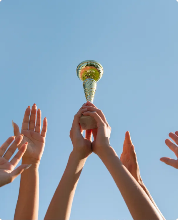 Hands reaching up to hold a gold trophy against a clear blue sky.