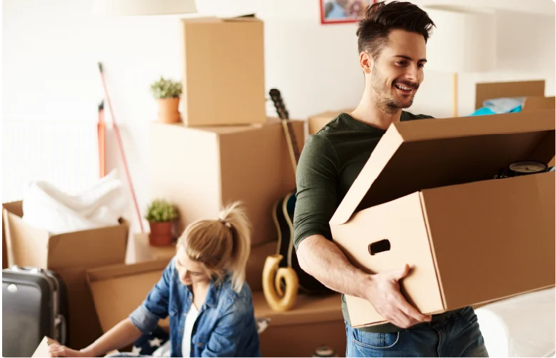 A happy young couple carrying cardboard boxes while moving into a new apartment.