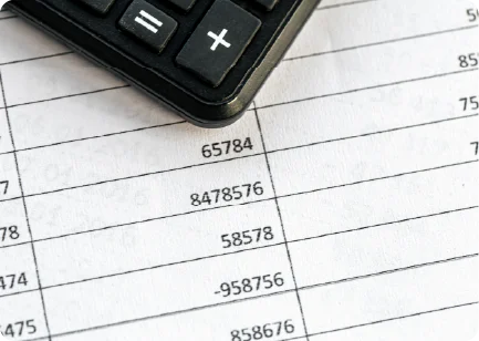 A close-up of a calculator sitting on top of a financial document with rows of numbers.