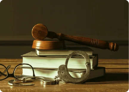 A wooden judge's gavel resting on stacked books next to a pair of metal handcuffs.