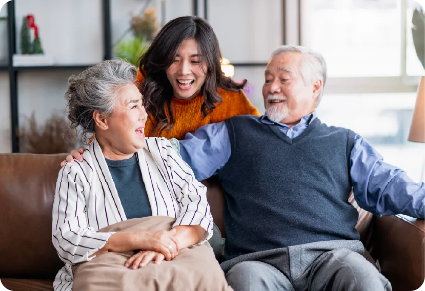 A joyful elderly couple laughing with a younger woman in a living room.