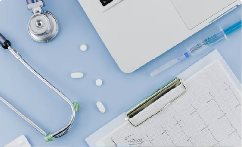 A flat lay of a medical stethoscope, clipboard, laptop, and pills on a clean blue background, representing healthcare services.