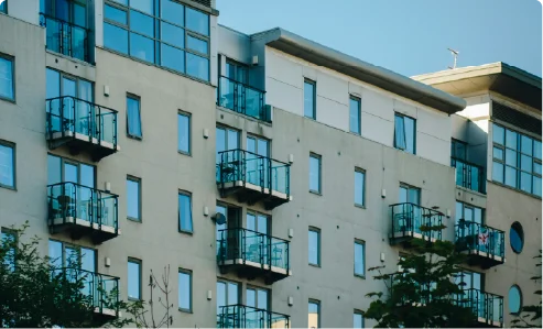 A modern residential apartment building with glass balconies under a bright blue sky.