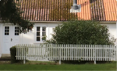 A classic white suburban house with an orange tiled roof behind a white wooden picket fence.