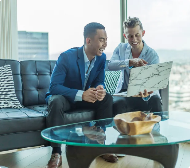 Two business professionals sitting on a leather sofa looking at a laptop computer together during a friendly consultation.