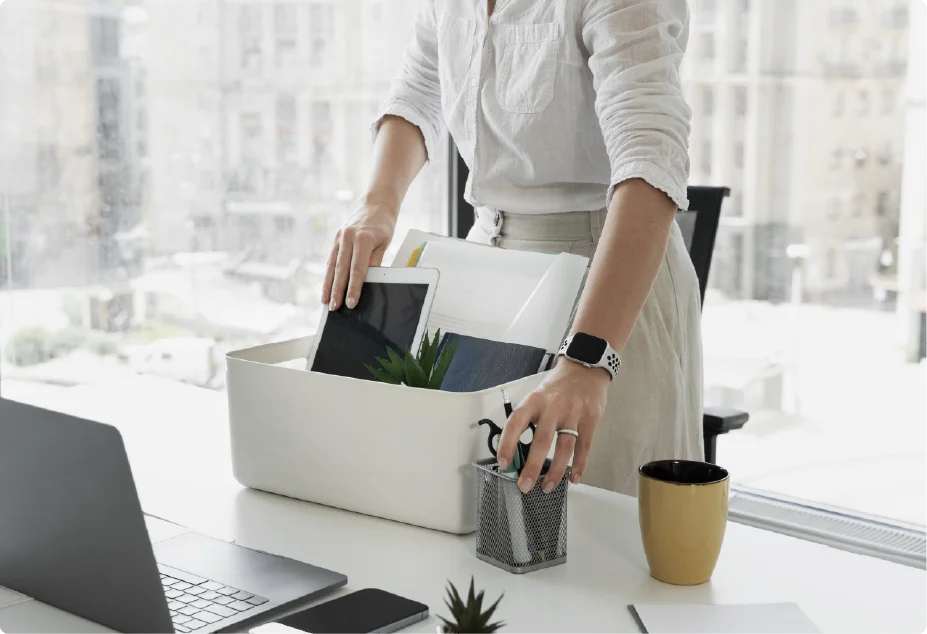 An employee packing their personal belongings into a cardboard box at an office desk, representing resignation or job change.